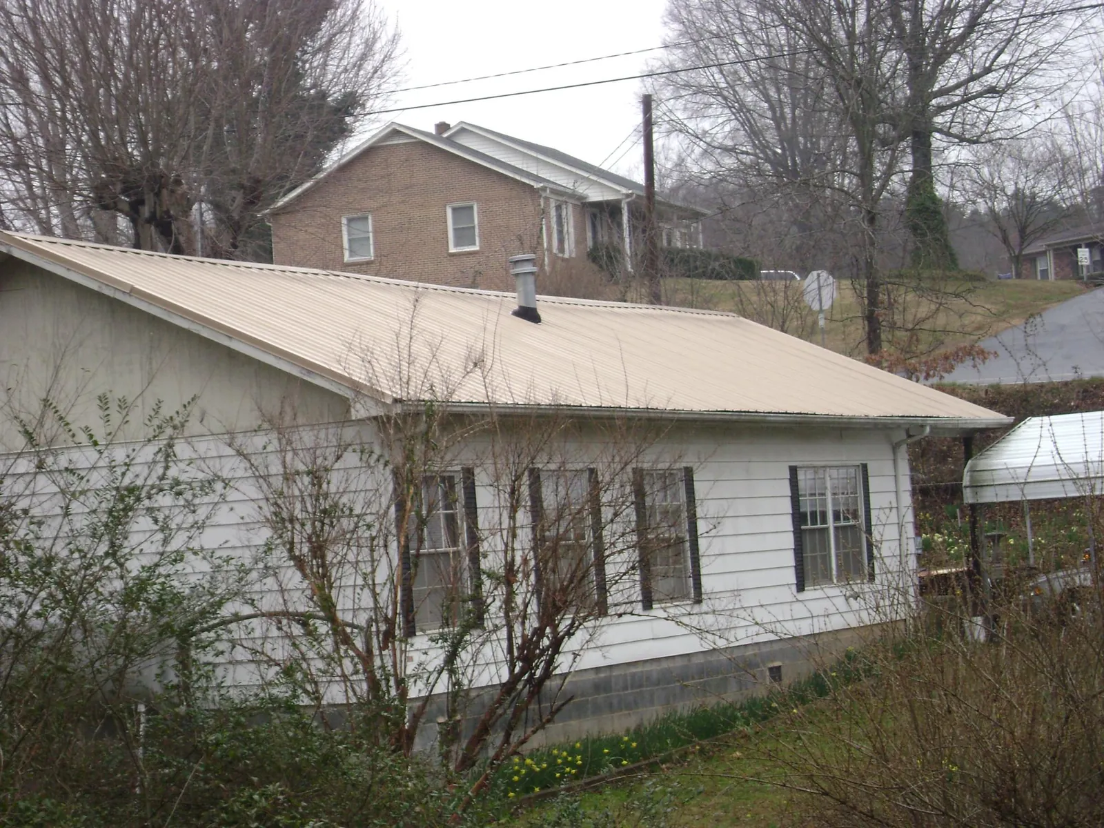 Tan metal roof on a white sided house set into a hillside — Commercial Roofing by Roofing Brothers in Silver City